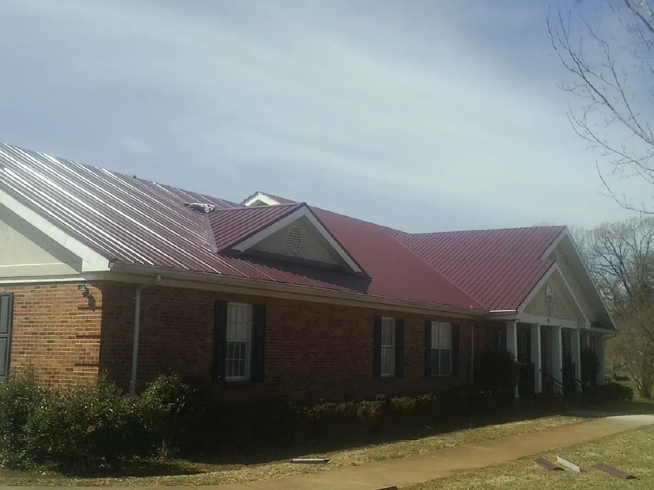Red metal roof with gabled entries on a long brick building, from a Hail Damage Roof Repair job in Velpen