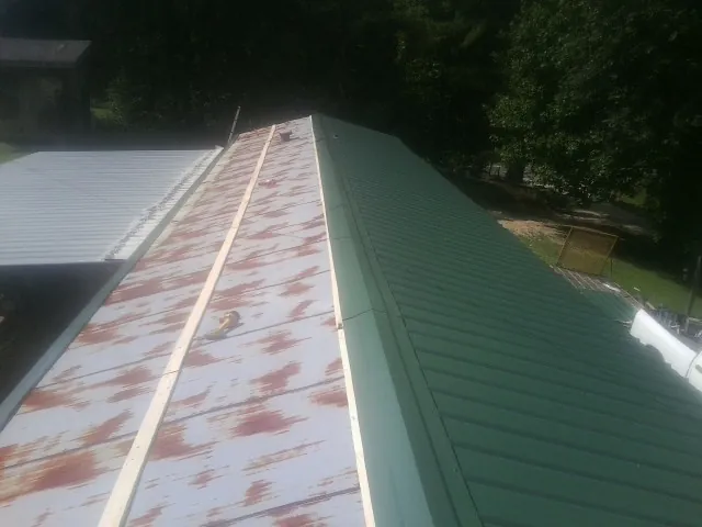 Old rusted panels beside newly installed green metal roofing — Wind Damage Roof Repair by Roofing Brothers in Velpen