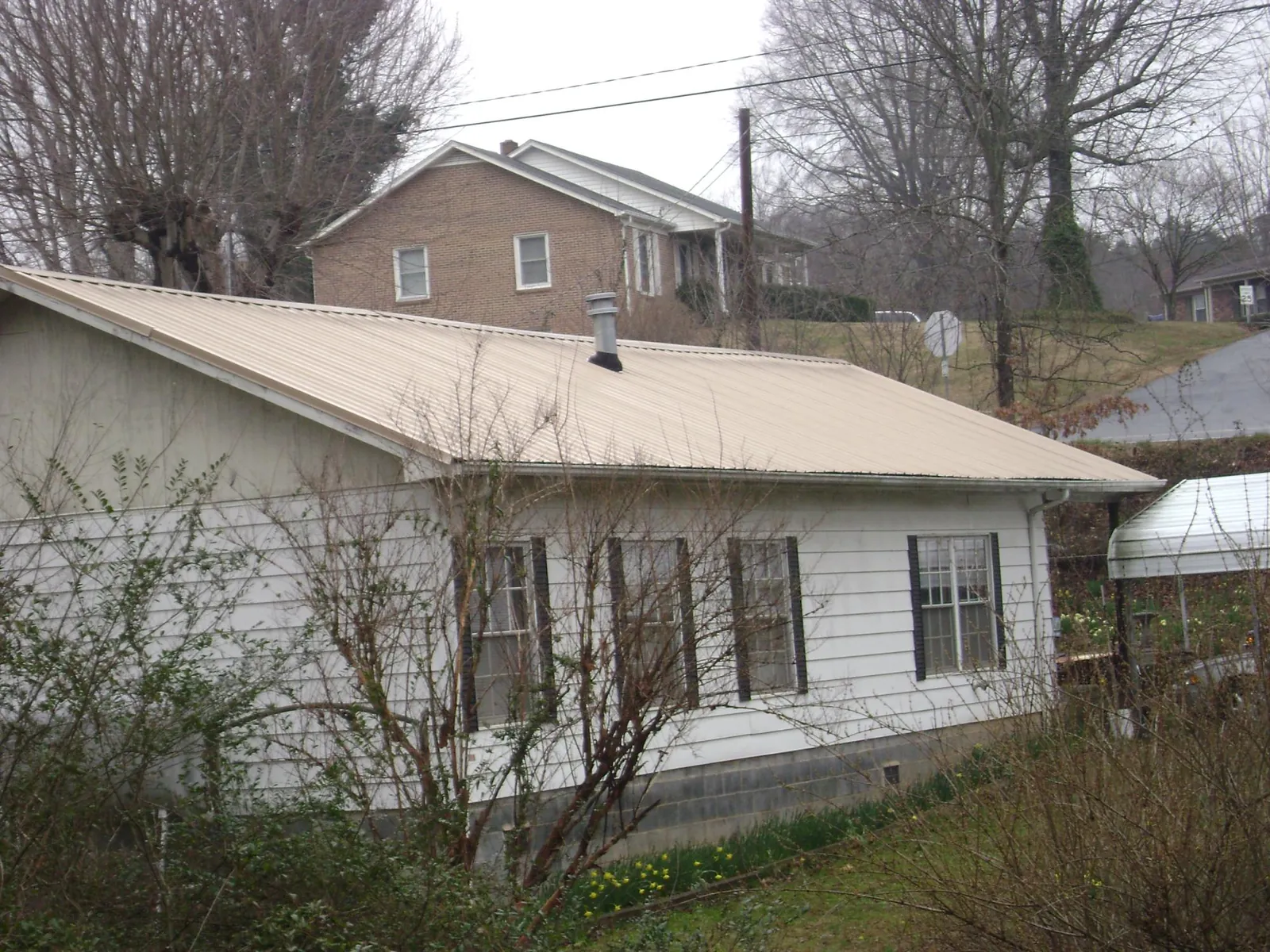 Tan metal roof on a white sided house set into a hillside — Commercial Roofing by Roofing Brothers in Velpen